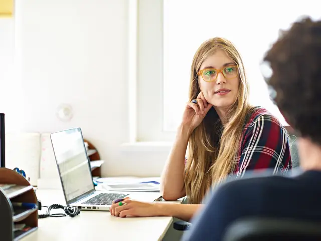 Kvinne foran en PC ser på en annen person