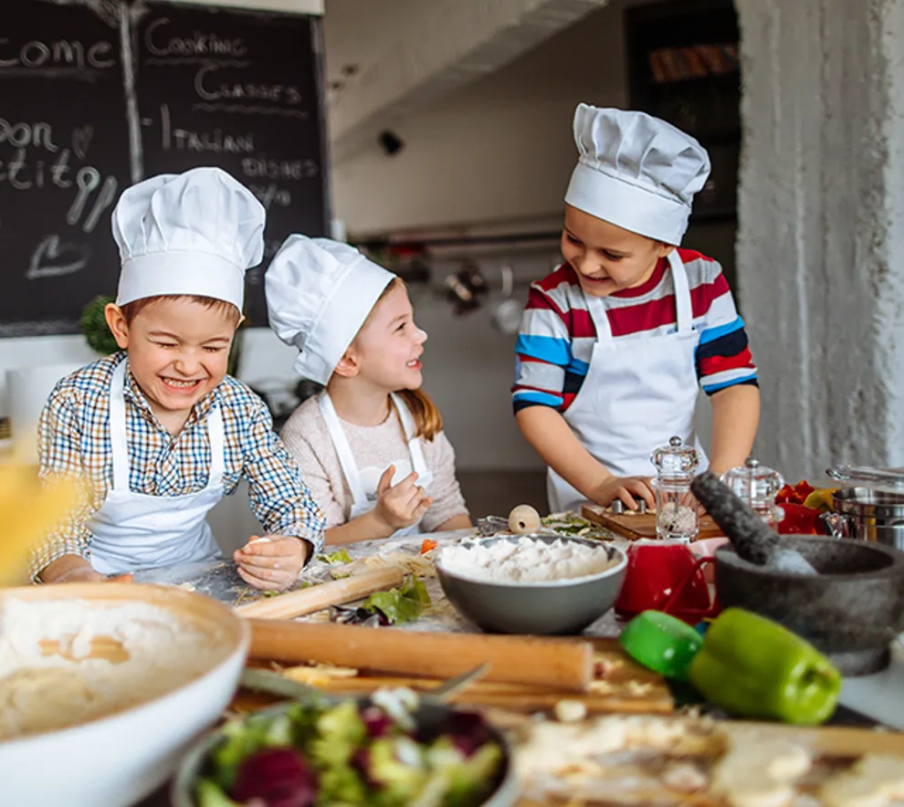 Tre barn som lager mat og er glade