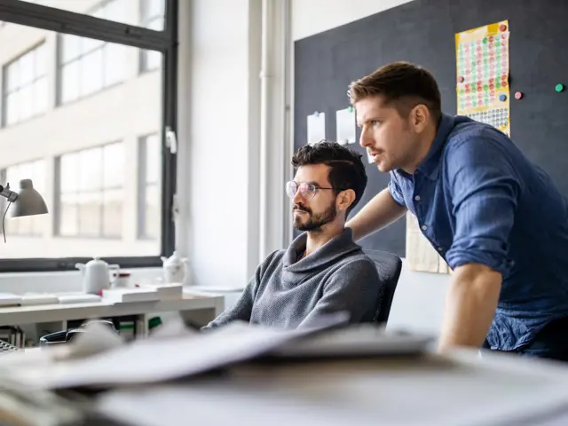 Illustrasjonsbilde av en mann som viser en kollega noe på datamaskinen