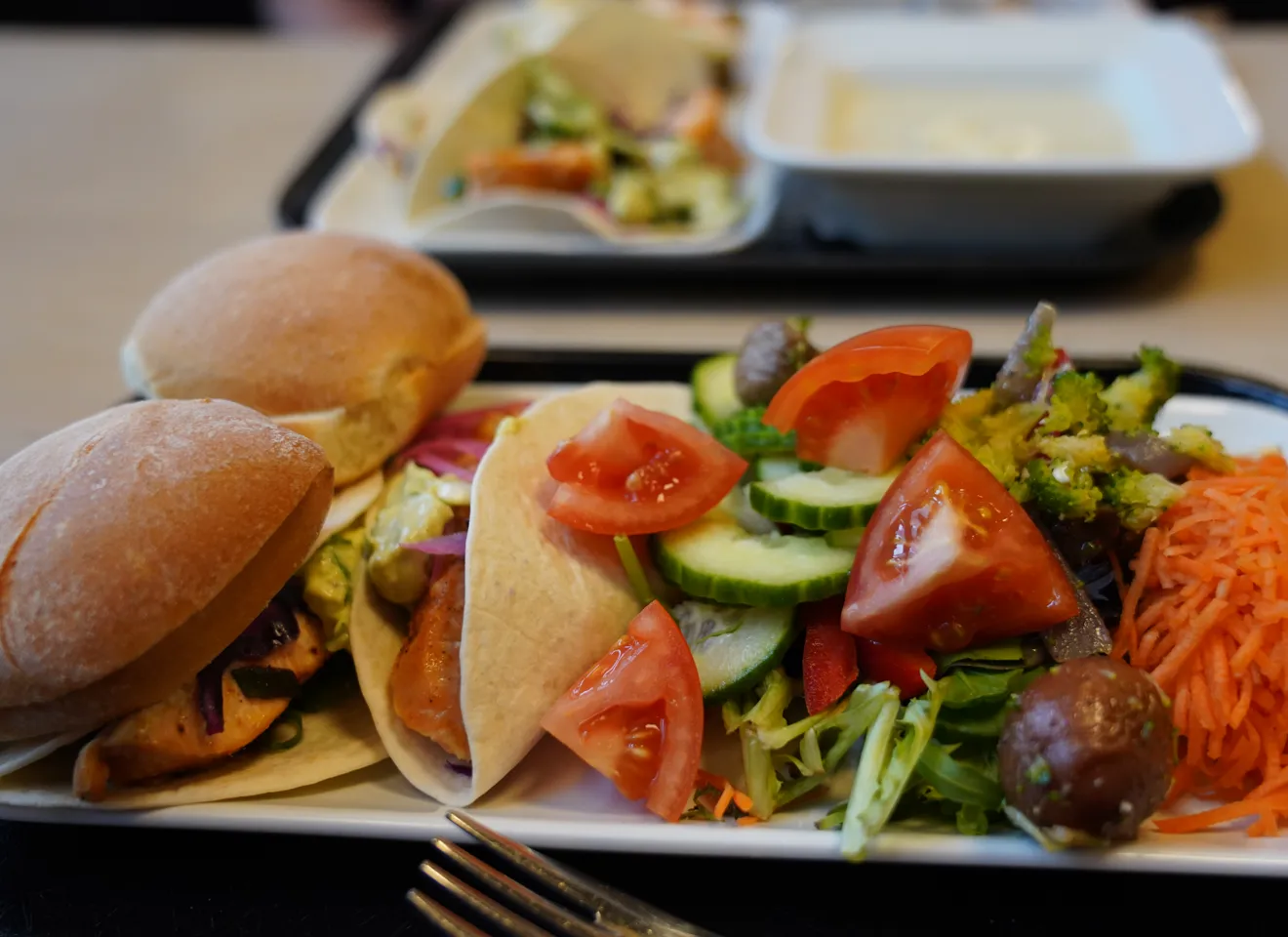 Nærbilde av frokost eller lunsj på et brett i en kantine med salat og rundstykker
