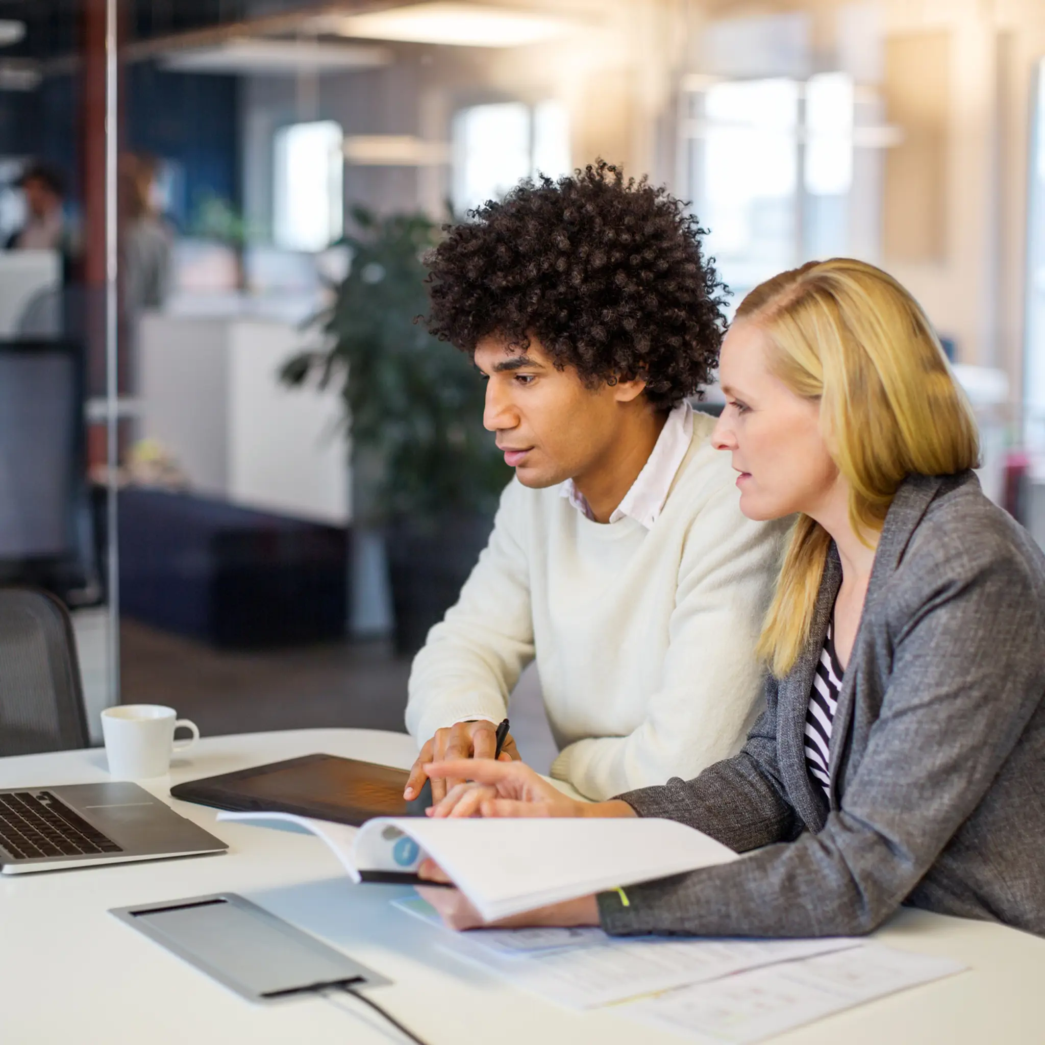 Ung kvinne og ung mann med dokumenter og laptop ved et bord