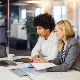 Ung kvinne og ung mann med dokumenter og laptop ved et bord