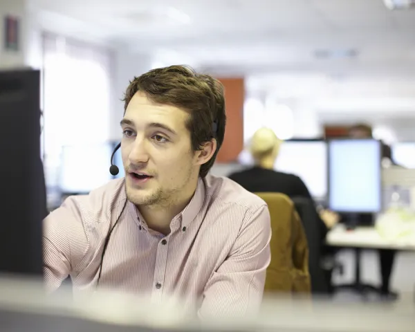 En ung mann med headsett sitter foran en PC og snakker med en kunde på telefon