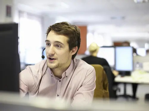En ung mann med headsett sitter foran en PC og snakker med en kunde på telefon