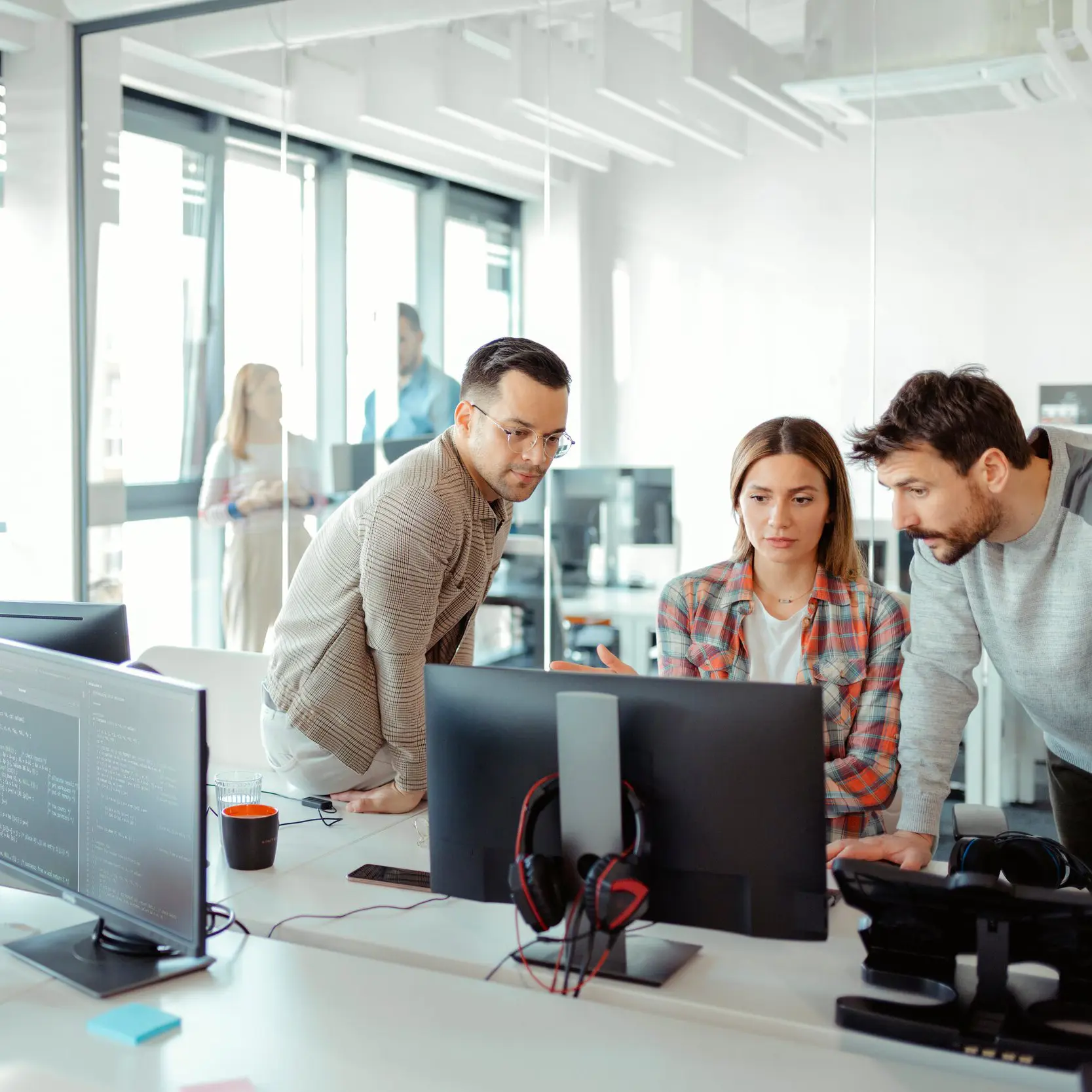 To menn og en kvinne i et kontorlanskap som ser på en pc-skjerm