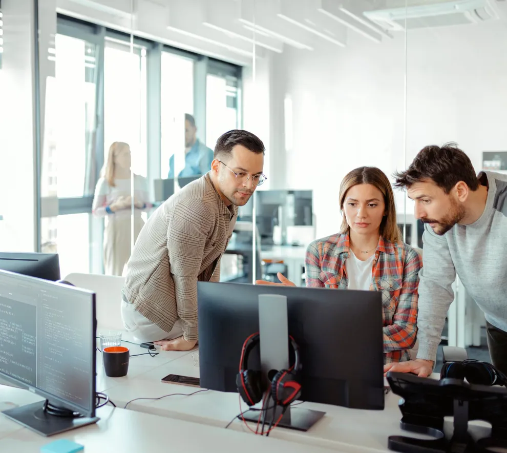 To menn og en kvinne i et kontorlanskap som ser på en pc-skjerm