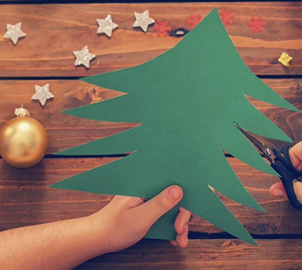 Et barn som klipper ut et juletre i grønt papir