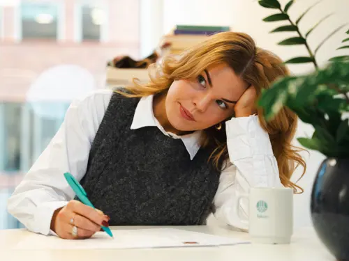 Ung kvinne med penn og papir på kontor