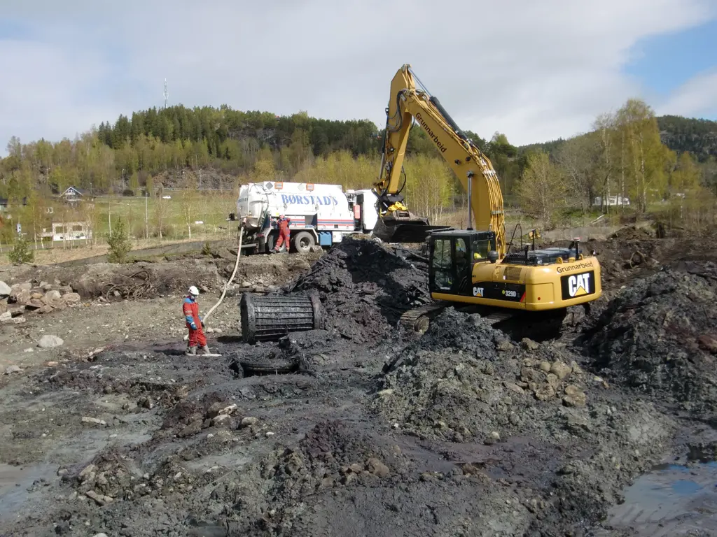 Gravemaskin i sving med å grave på et jorde