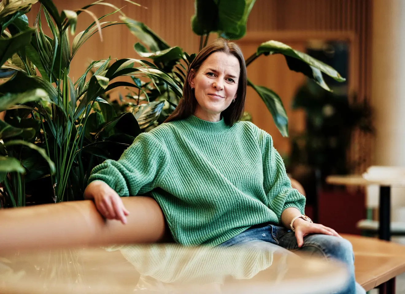 Kvinne i grønn genser i sofa med planter rundt