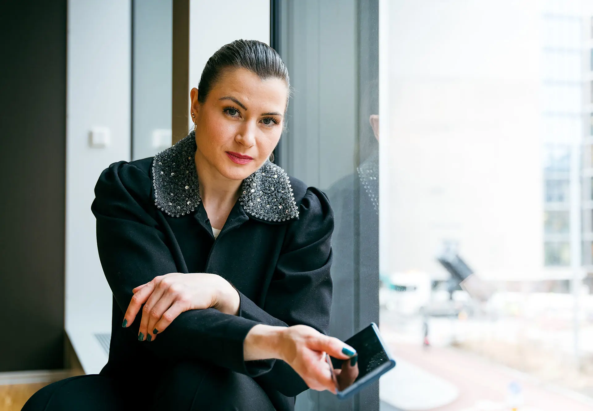 Elisabet Haugsbø med svart jakke, hvit topp, nøytralt ansiktsuttrykk, med mobiltelefonen i hånda 