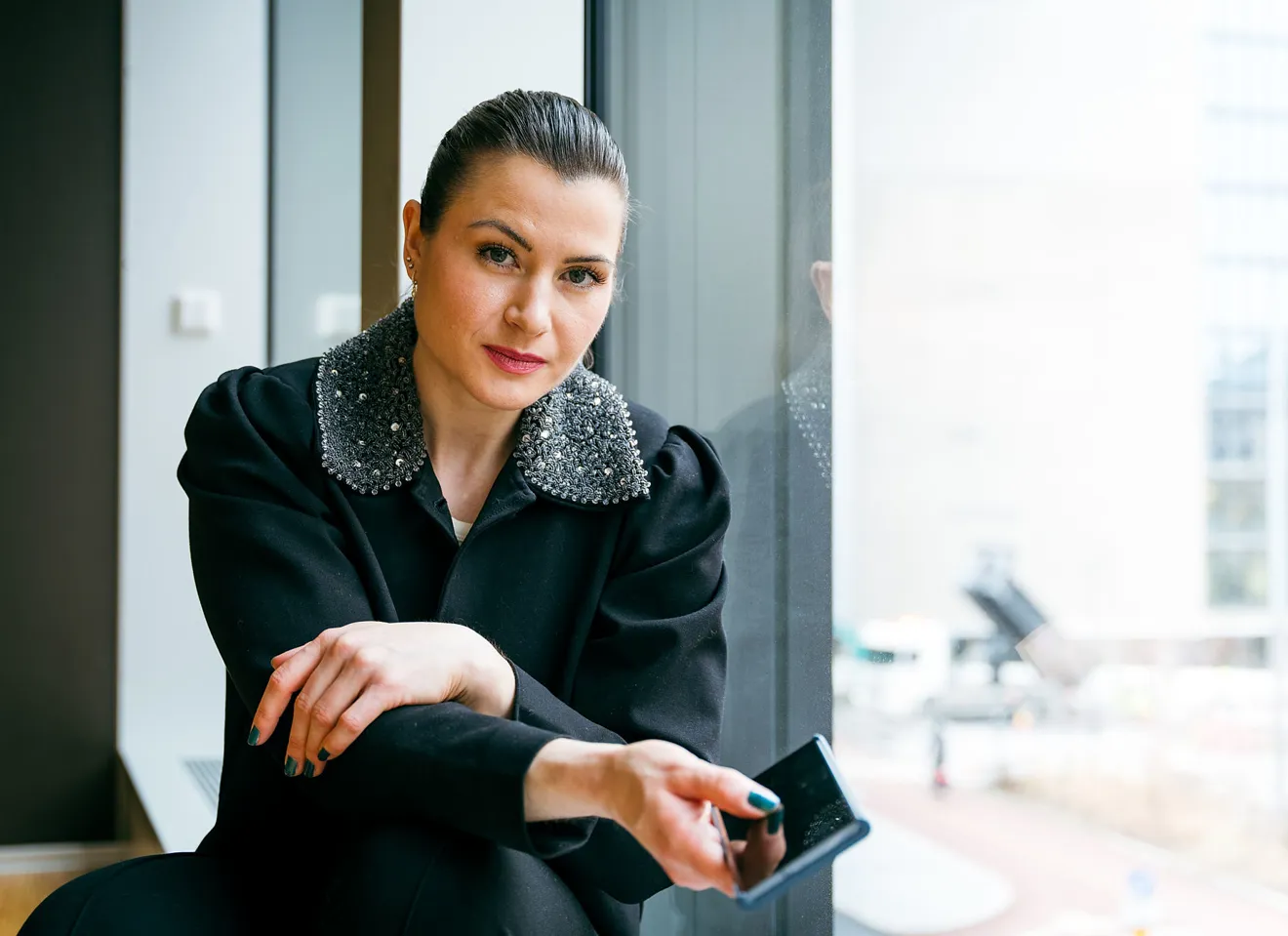 Elisabet Haugsbø med svart jakke, hvit topp, nøytralt ansiktsuttrykk, med mobiltelefonen i hånda