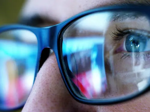 Nærbilde av øyer med briller og dataskjerm som reflekteres i brilleglass