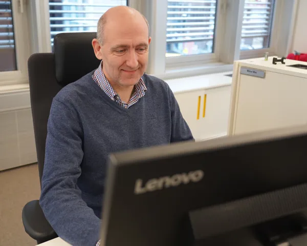 Anders Kvam sitter ved datamaskin og smiler