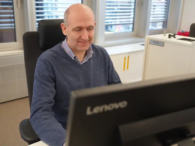 Anders Kvam sitter ved datamaskin og smiler