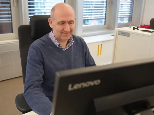Anders Kvam sitter ved datamaskin og smiler