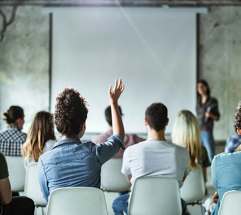Mennesker som sitter samlet i ett møte der en kvinne rekker opp hånden