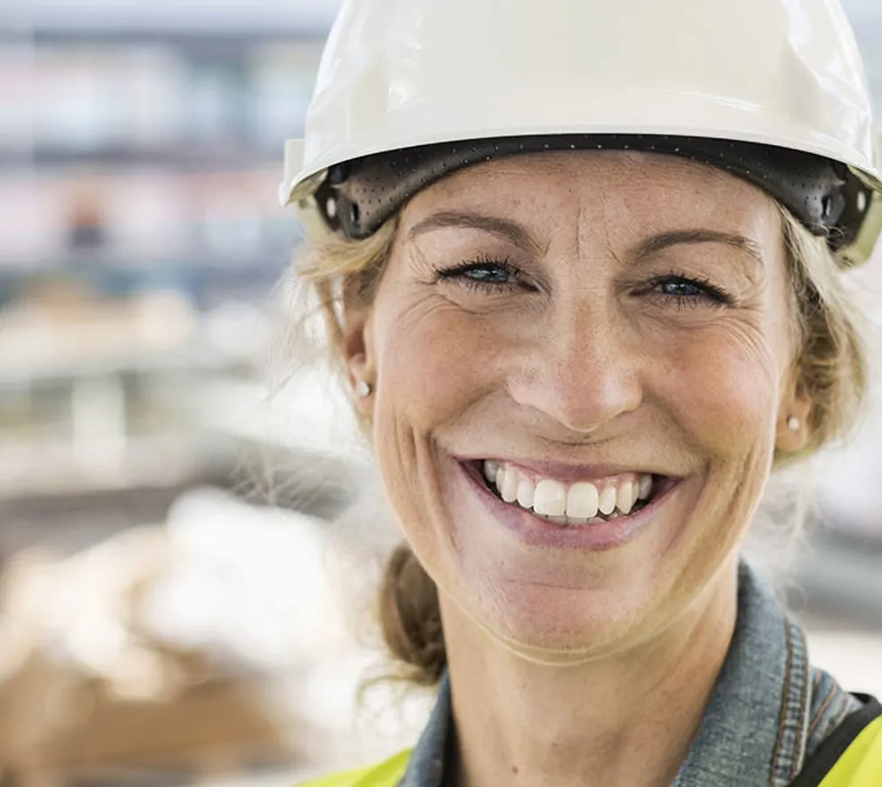 Smilende kvinne i gul hjelm på byggeplass.