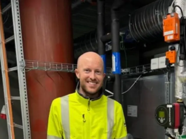 Mann står innendørs i arbeidsklær