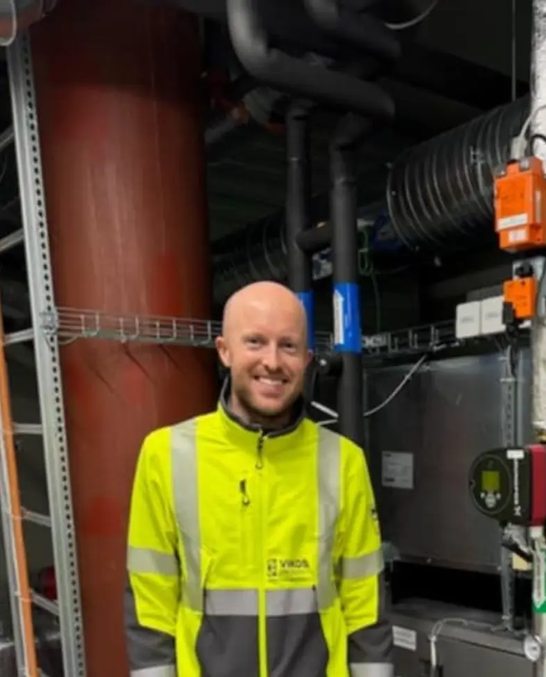 Mann står innendørs i arbeidsklær