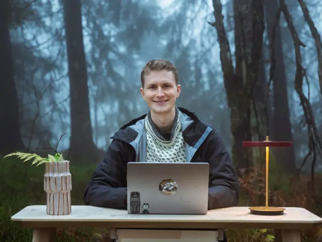 Mann med pc på bord og lampe i skogen