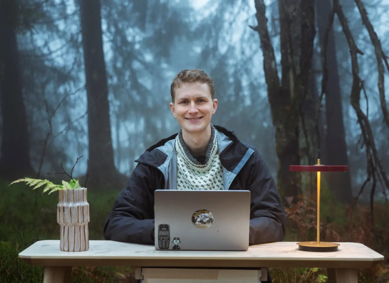 Mann med pc på bord og lampe i skogen