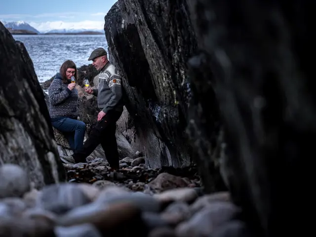 Kvinne og mann drikker fra glass mellom steinblokker
