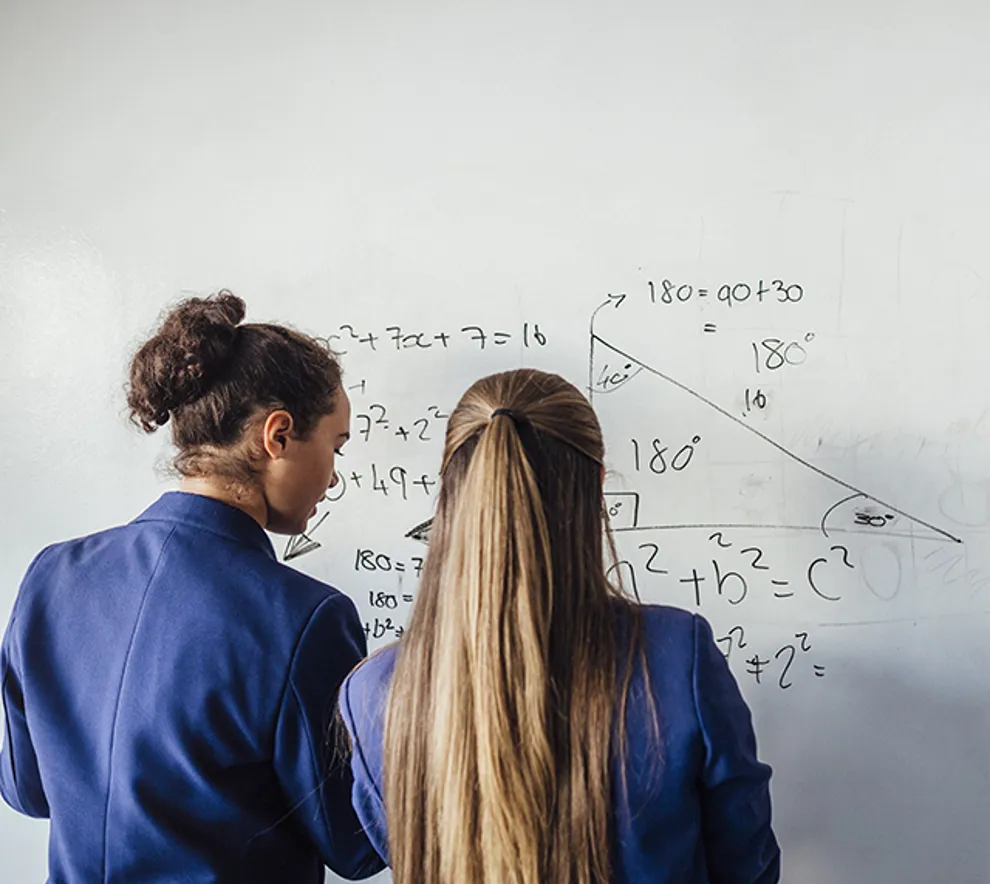To jenter som løser regnestykker på tavlen