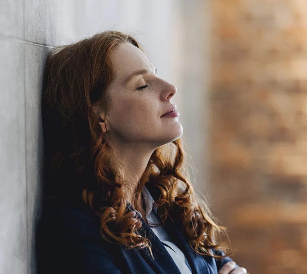 Kvinne med øynene lukket som lener seg mot en vegg