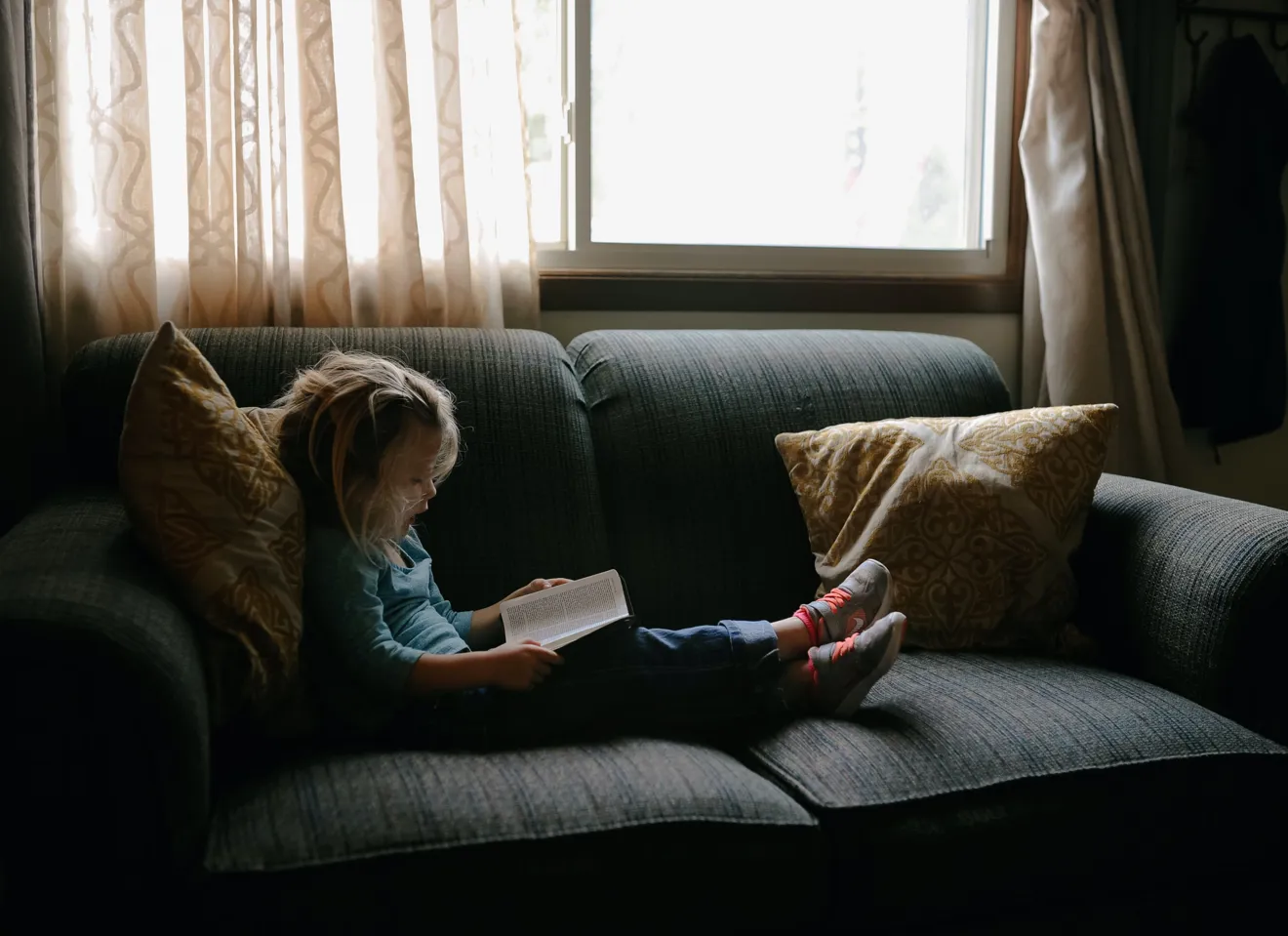 En liten jente sitter i en sofa og leser bok