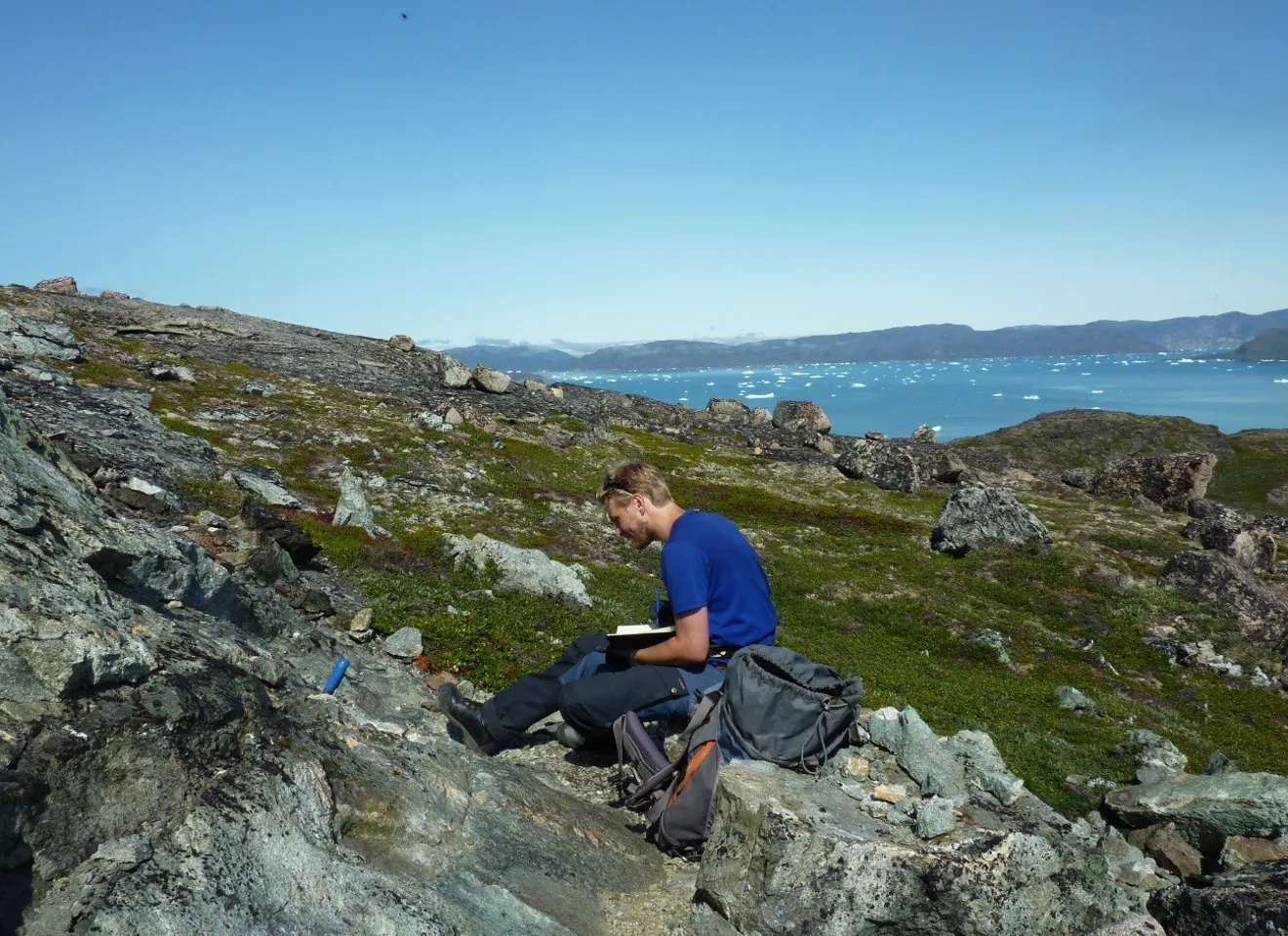 Emil som sitter på steiner i Grønland og studerer