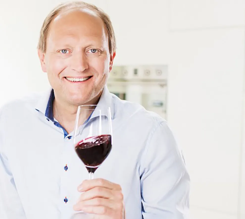 En mann som smiler med et glass rødvin i hånden
