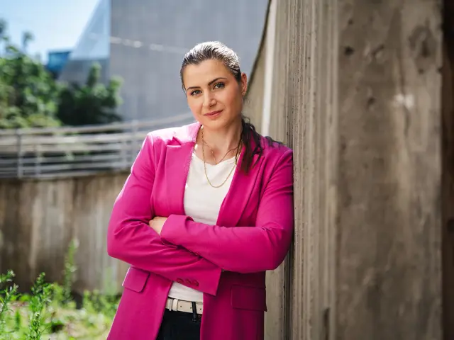 Elisabet Haugsbø smiler med rosa dressjakke, lener seg mot en betongvegg utendørs