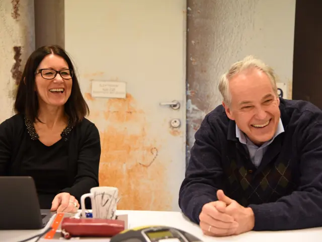 Bjerge og Skjeggerud ved et bord som smiler og ler