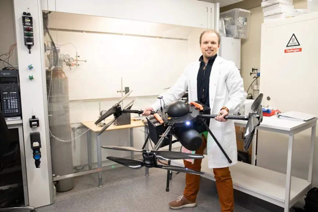 Jørgen Apeland i hvit laborfrakk i et verksted holder en stor sort drone
