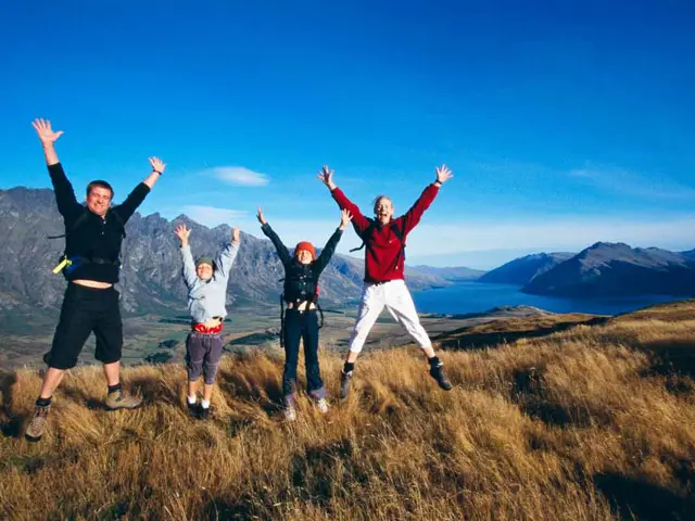 Illustrasjonsbilde av en familie med to voksne og to barn ute på tur hopper og smiler til kamera