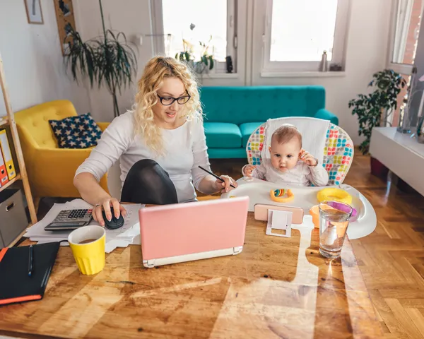 En kvinne med småbarn og laptop og hjemmekontor i stuen