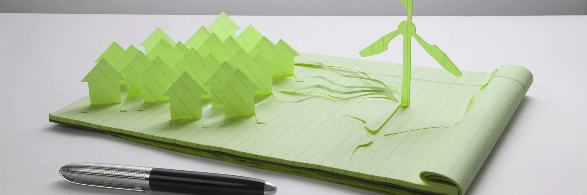 Pen og skirveblokk, mange hus og en vindmølle i papir stå opp fra skriveblokken
