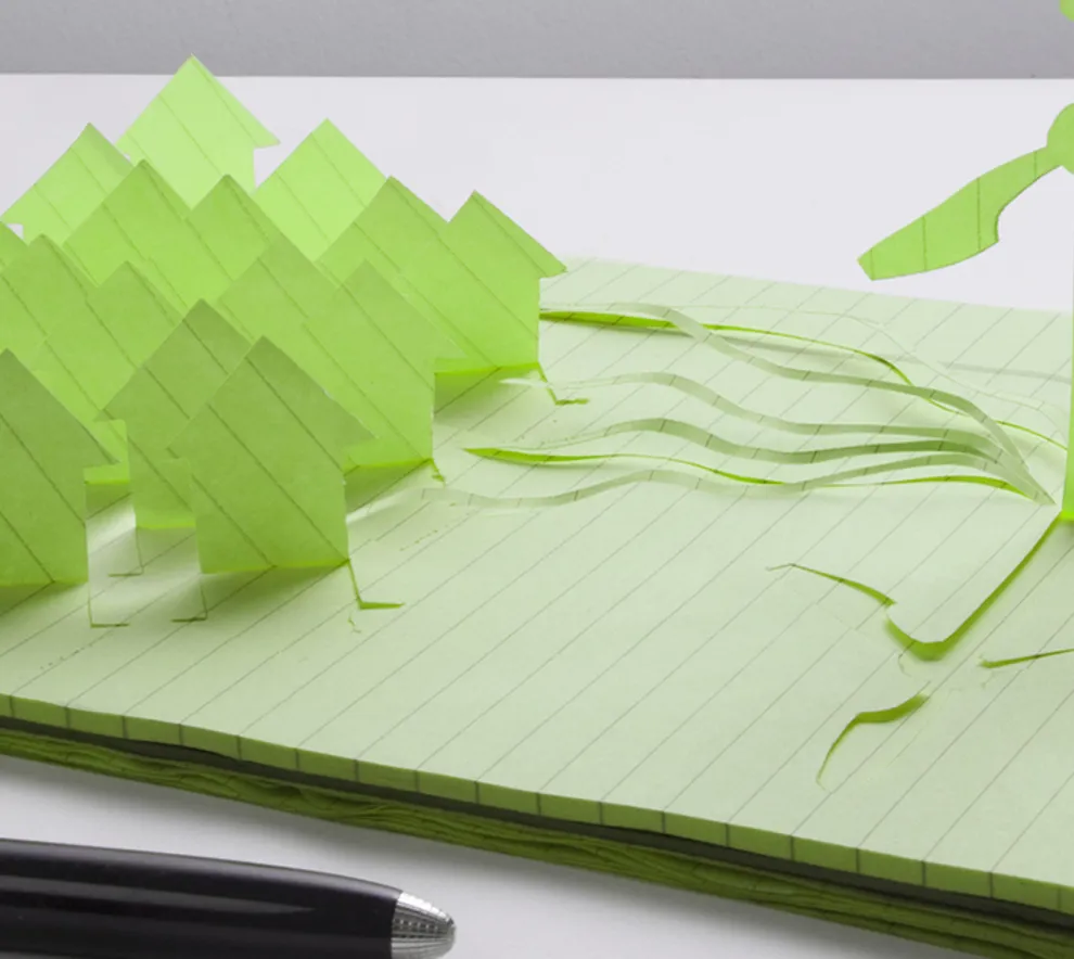 Pen og skirveblokk, mange hus og en vindmølle i papir stå opp fra skriveblokken