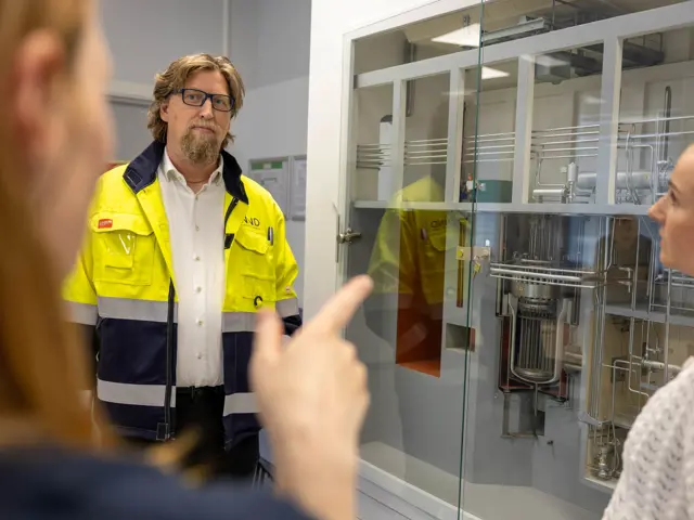 Mann i gult snakker med 2 kvinner i teknisk rom