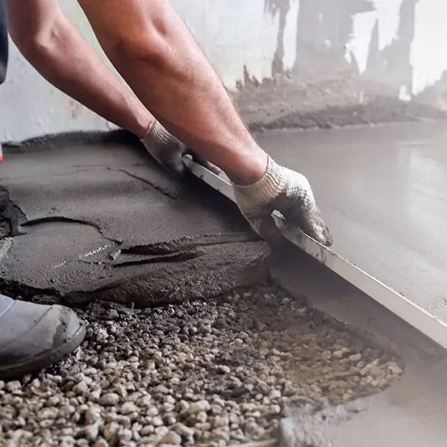 Betongarbeider som drar betong utover gulvflaten så det blir jevnt