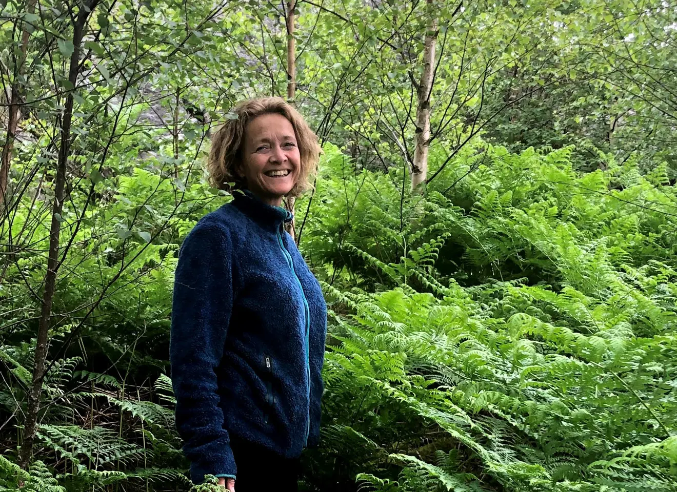 Hanne Etterlid i skogen foran en stor busk