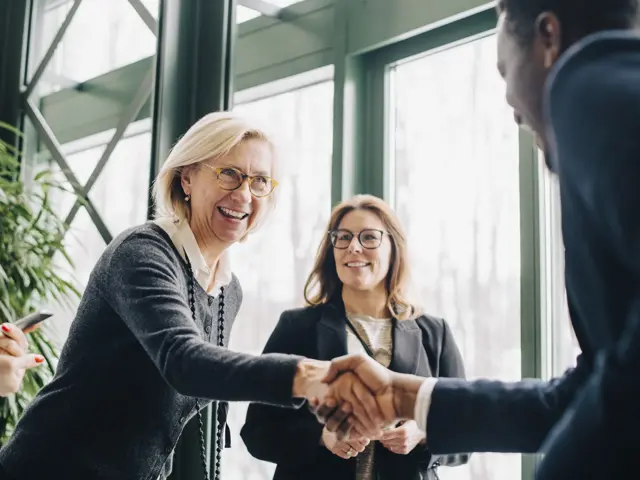Bilde av to personer som håndhilser, med en tredje person i bakgrunnen