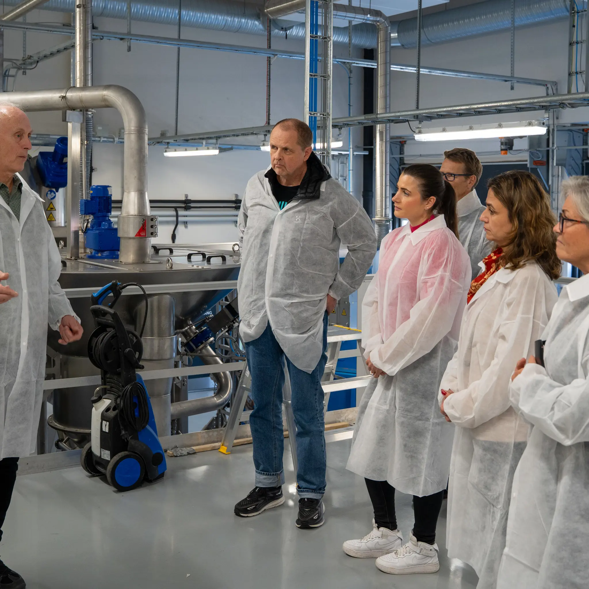 seks personer i hvite beskyttelsesfrakker i industrilokale