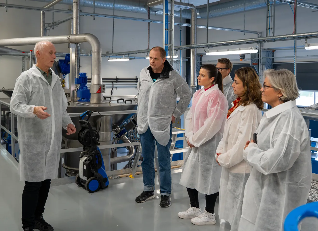 seks personer i hvite beskyttelsesfrakker i industrilokale