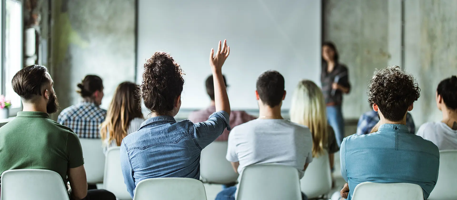 En forsamling mennesker som hører på en foredragsholder og en kvinne som rekker opp hånden 