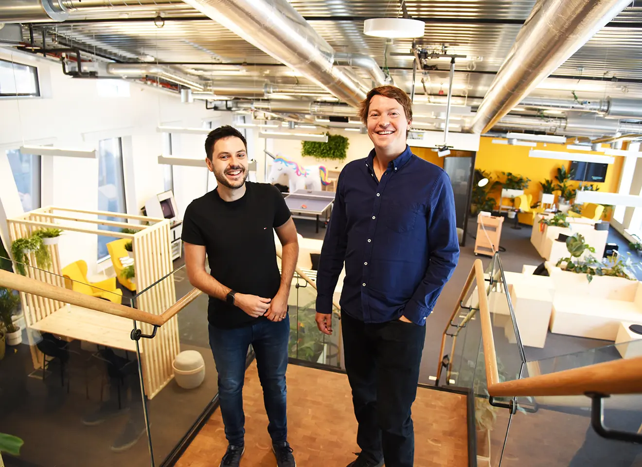 Martin Skarbø Sangolt og Christian Mikalsen står i toppen av en trapp i et kontorlokale med gule vegger