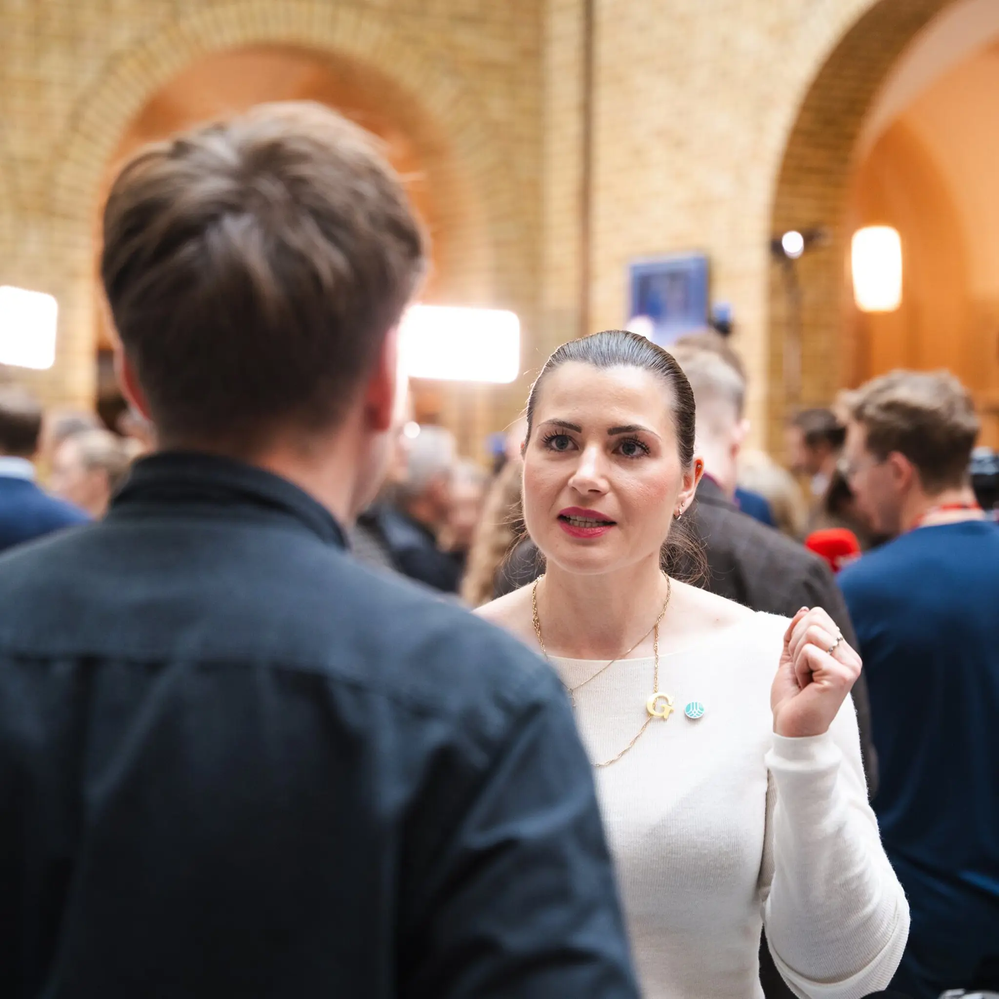 Elisabet Haugsbø i samtale med en mann med ryggen til, i hvit genser og med Tekna-pin. I vandrehallen på Stortinget 