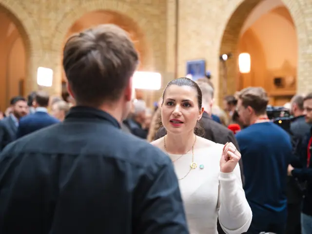 Elisabet Haugsbø i samtale med en mann med ryggen til, i hvit genser og med Tekna-pin. I vandrehallen på Stortinget 