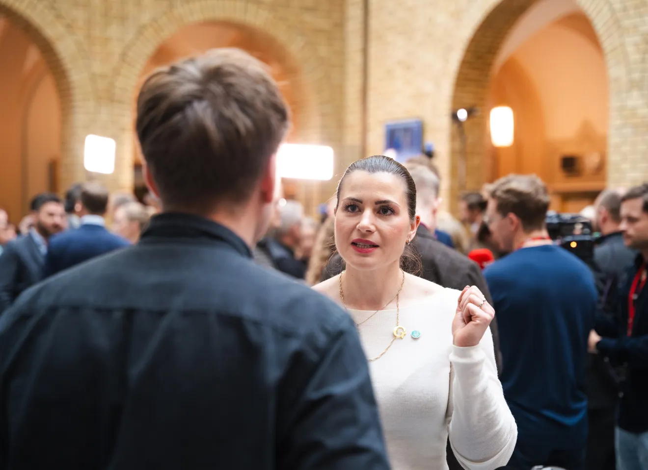 Elisabet Haugsbø i samtale med en mann med ryggen til, i hvit genser og med Tekna-pin. I vandrehallen på Stortinget